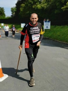 Ismail Patel smiles as he competes in a running event, aided by a stick.